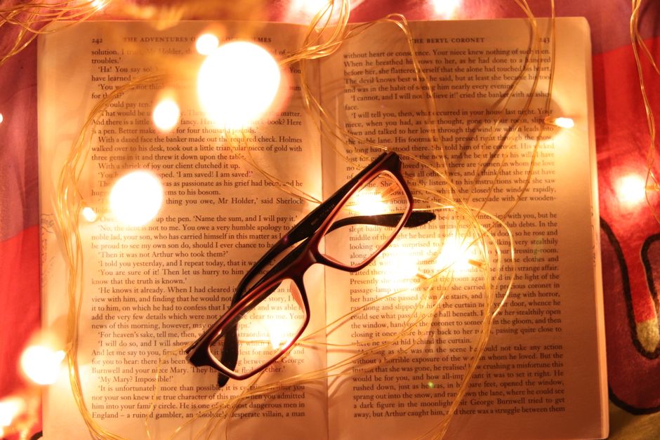 Artistic composition of an open book, spectacles, and glowing fairy lights creating a warm, inviting atmosphere.